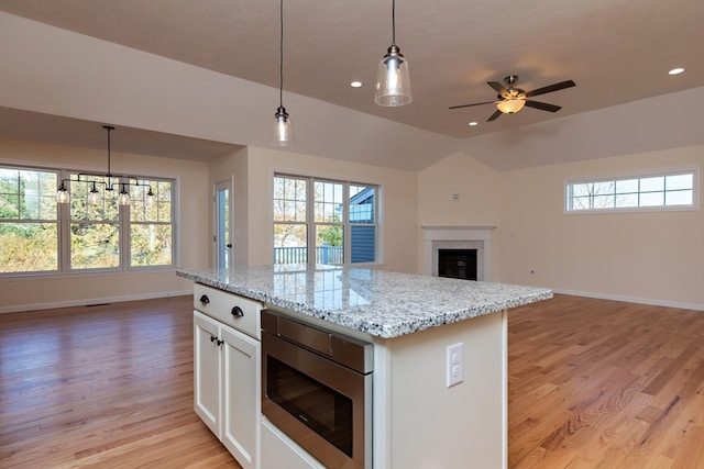 kitchen with stainless steel microwave, white cabinetry, pendant lighting, and a wealth of natural light