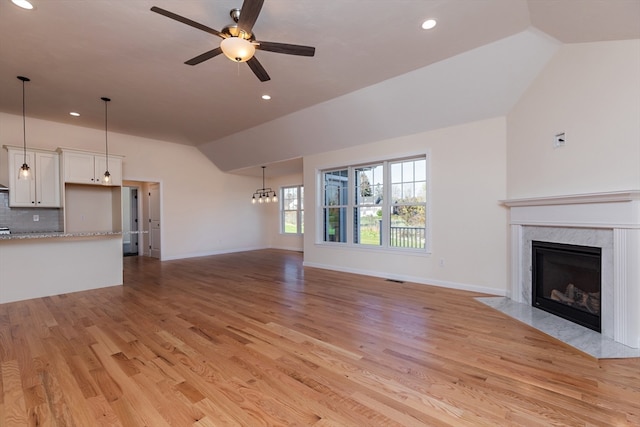 unfurnished living room with lofted ceiling, a high end fireplace, light wood-type flooring, and ceiling fan