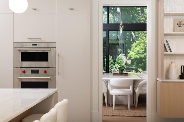 kitchen with double oven, modern cabinets, and light stone counters