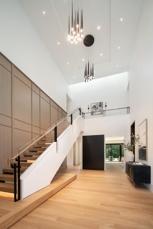 interior space with stairs, light wood-type flooring, a towering ceiling, and an inviting chandelier