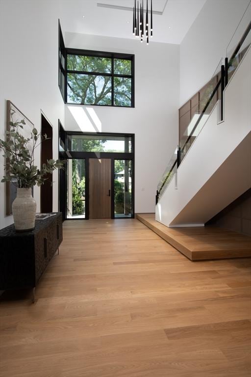 foyer entrance featuring a towering ceiling, light wood finished floors, and stairs