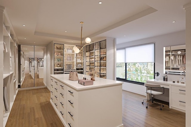 spacious closet featuring light wood-type flooring, a tray ceiling, and built in desk