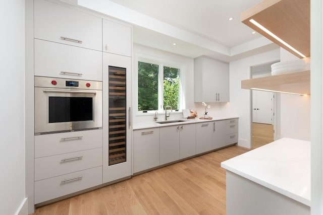 kitchen featuring light wood-style flooring, oven, a sink, white cabinets, and light countertops