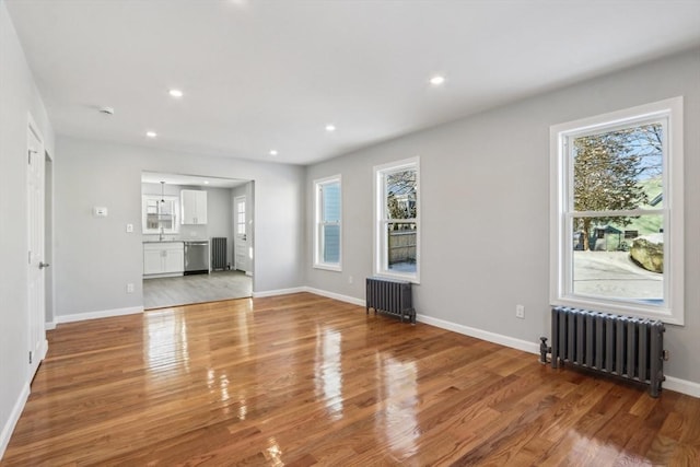 unfurnished living room with wood-type flooring, radiator, and a wealth of natural light