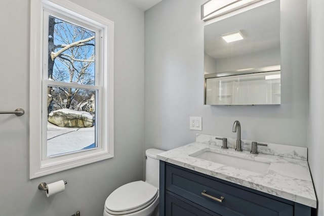 bathroom featuring a shower with door, vanity, and toilet