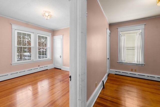 interior space with ornamental molding, a baseboard heating unit, and hardwood / wood-style floors