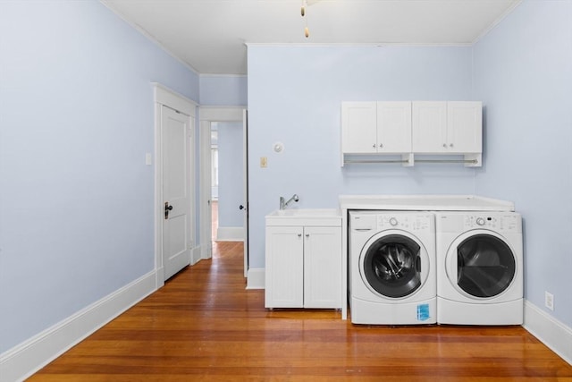 washroom featuring sink, cabinets, hardwood / wood-style flooring, ornamental molding, and washing machine and dryer