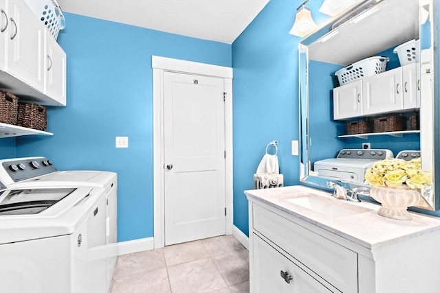 clothes washing area featuring light tile patterned floors, washing machine and dryer, a sink, baseboards, and cabinet space