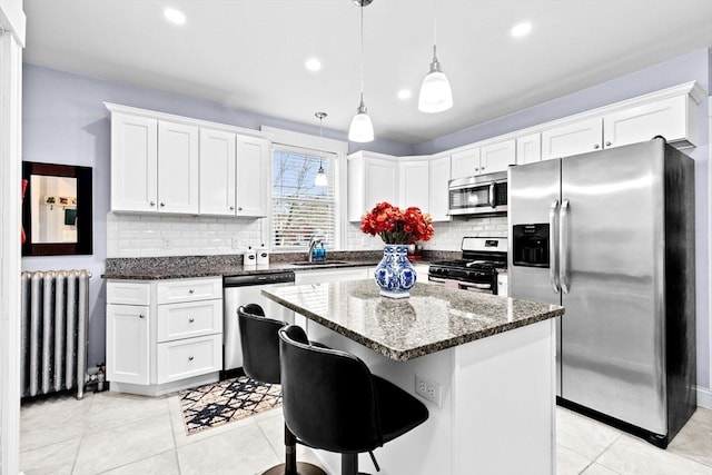 kitchen featuring stainless steel appliances, a kitchen island, white cabinetry, dark stone counters, and radiator heating unit