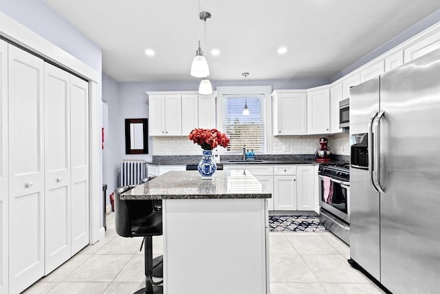 kitchen featuring light tile patterned floors, radiator heating unit, appliances with stainless steel finishes, white cabinets, and a kitchen island