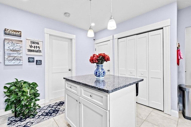 kitchen featuring white cabinets, dark stone countertops, a center island, hanging light fixtures, and light tile patterned flooring