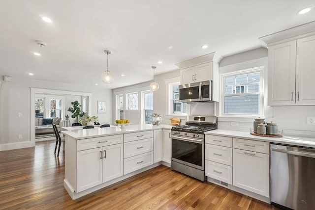 kitchen with stainless steel appliances, wood finished floors, a peninsula, and light countertops