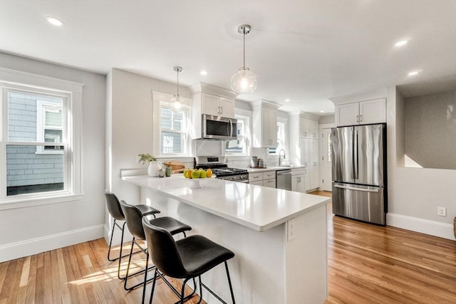 kitchen featuring light countertops, appliances with stainless steel finishes, light wood-style flooring, and a breakfast bar