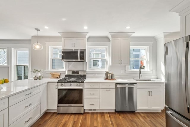 kitchen with white cabinets, appliances with stainless steel finishes, wood finished floors, light countertops, and a sink