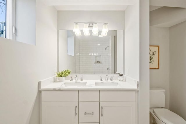 full bathroom featuring a tile shower, double vanity, a sink, and toilet