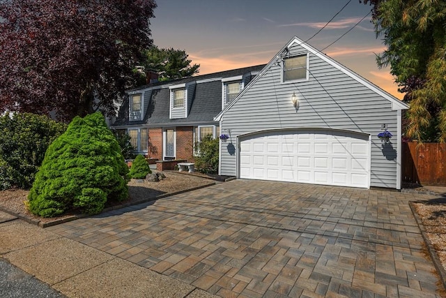 view of front of home with a garage, roof with shingles, brick siding, and decorative driveway