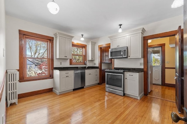 kitchen featuring dark countertops, a sink, radiator heating unit, stainless steel appliances, and light wood-style flooring