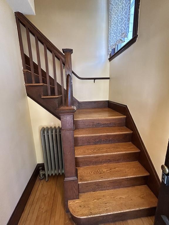 stairway featuring radiator, baseboards, and hardwood / wood-style flooring