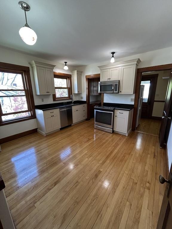 kitchen featuring decorative light fixtures, dark countertops, appliances with stainless steel finishes, baseboards, and light wood finished floors