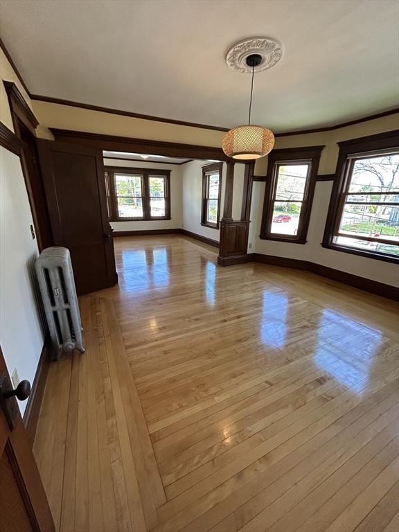 unfurnished dining area featuring light wood-type flooring, baseboards, crown molding, and radiator heating unit