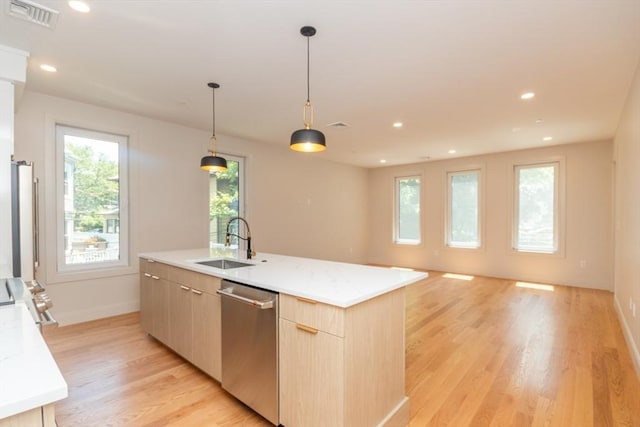 kitchen featuring dishwasher, sink, decorative light fixtures, a kitchen island with sink, and light brown cabinetry