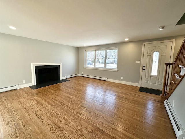 unfurnished living room with a wealth of natural light, hardwood / wood-style flooring, and a baseboard heating unit