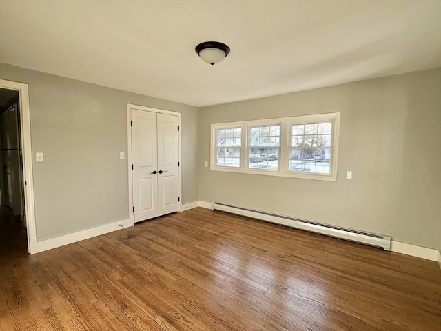 unfurnished bedroom featuring hardwood / wood-style floors, a closet, and a baseboard heating unit