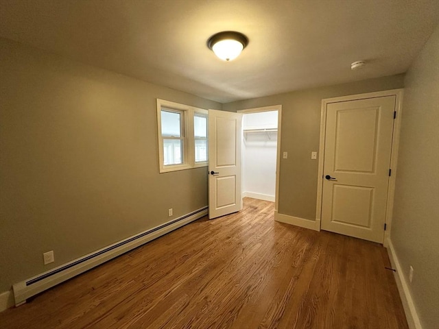 unfurnished bedroom with wood-type flooring, a walk in closet, a closet, and a baseboard heating unit