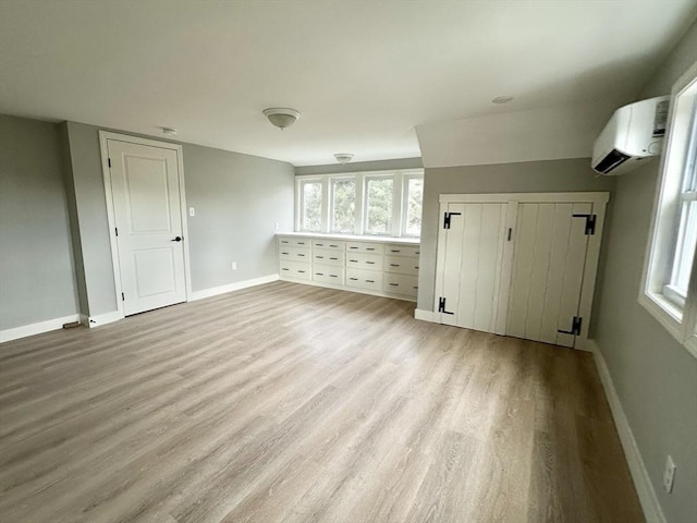 additional living space featuring a wall mounted air conditioner and light hardwood / wood-style flooring