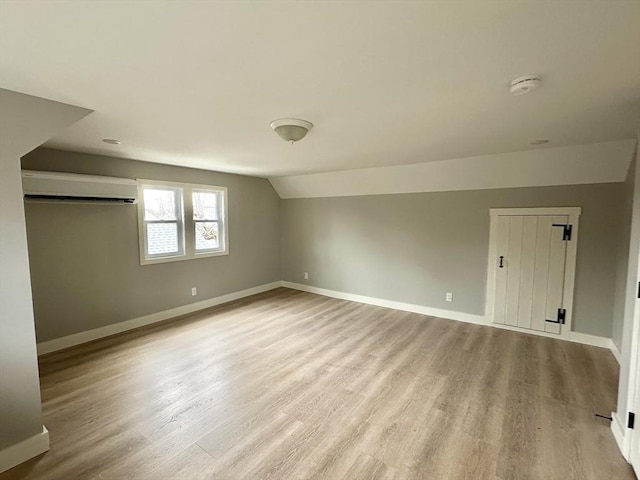 additional living space featuring a wall mounted air conditioner, light wood-type flooring, and lofted ceiling