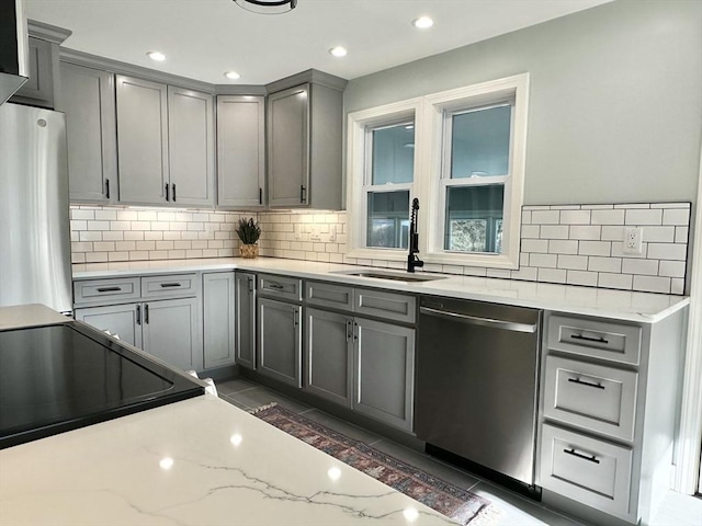 kitchen featuring backsplash, sink, gray cabinets, light stone countertops, and stainless steel appliances