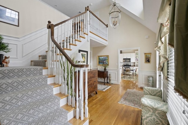 staircase featuring a wainscoted wall, a decorative wall, wood finished floors, and an inviting chandelier