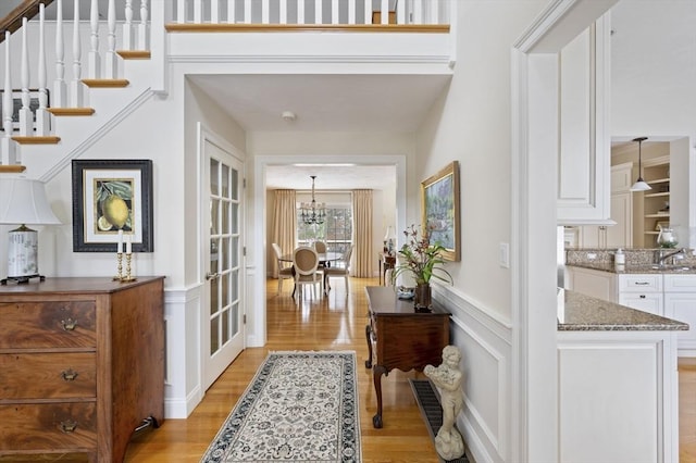 entrance foyer with light wood-type flooring, stairway, wainscoting, and a decorative wall