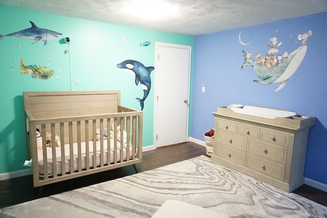 bedroom featuring dark wood-type flooring, a nursery area, and a textured ceiling