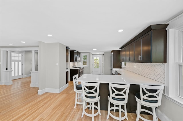 kitchen featuring light wood-type flooring, tasteful backsplash, kitchen peninsula, sink, and a breakfast bar area