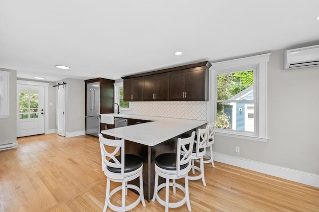 kitchen with dark brown cabinets, kitchen peninsula, an AC wall unit, a breakfast bar area, and light hardwood / wood-style floors