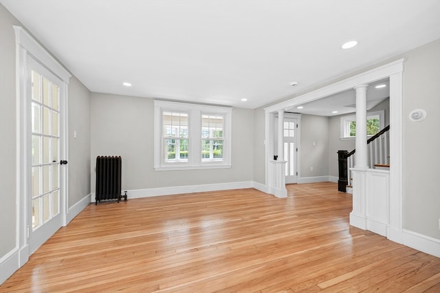 unfurnished living room with light wood-type flooring, radiator heating unit, and ornate columns