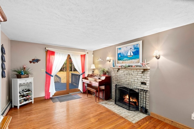 living room with a brick fireplace, wood-type flooring, a textured ceiling, and a baseboard radiator