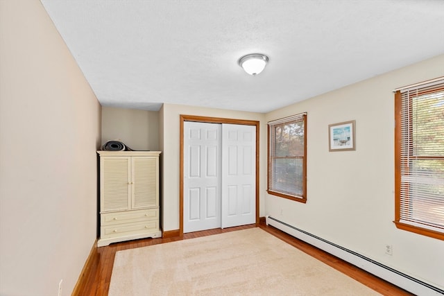 unfurnished bedroom featuring a closet, light wood-type flooring, a textured ceiling, and a baseboard radiator