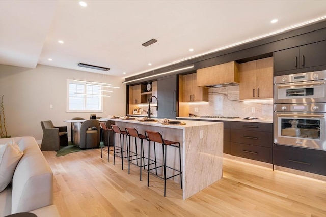 kitchen with sink, stainless steel appliances, light hardwood / wood-style floors, a breakfast bar area, and a kitchen island with sink