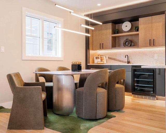 bar with light brown cabinets, beverage cooler, and light hardwood / wood-style floors