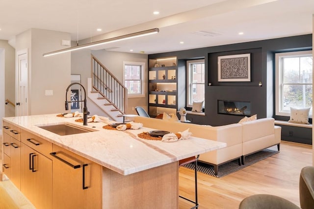 kitchen featuring light brown cabinetry, light wood-type flooring, a kitchen breakfast bar, light stone counters, and an island with sink