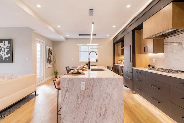 kitchen with a center island with sink, sink, decorative backsplash, decorative light fixtures, and light hardwood / wood-style floors