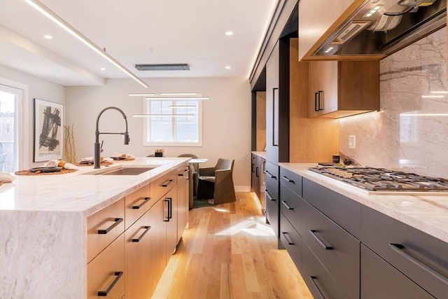 kitchen with light stone countertops, custom range hood, sink, light brown cabinets, and light hardwood / wood-style flooring