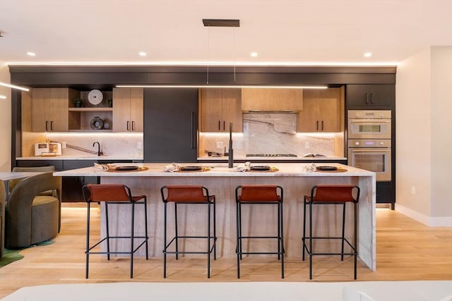 kitchen featuring a kitchen breakfast bar, light hardwood / wood-style floors, a kitchen island with sink, and double oven