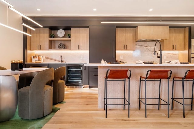 kitchen with a kitchen bar, decorative backsplash, light hardwood / wood-style flooring, and beverage cooler