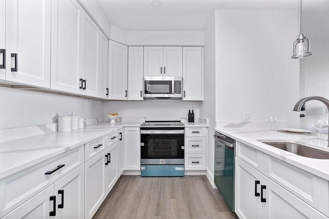 kitchen featuring sink, hanging light fixtures, light wood-type flooring, appliances with stainless steel finishes, and white cabinets