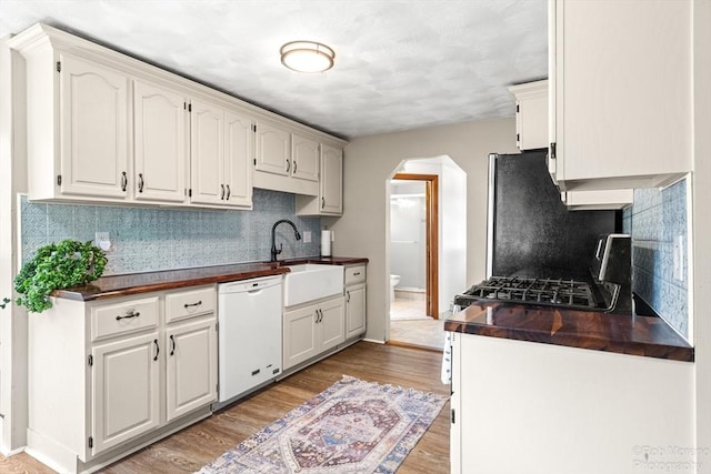 91 Bartholomew St, Peabody, MA 01960 - kitchen featuring white dishwasher, arched walkways, dark countertops, light wood-type flooring, and decorative backsplash