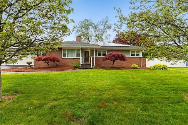 ranch-style house featuring a front lawn, roof mounted solar panels, a chimney, and brick siding