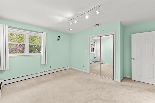unfurnished bedroom with a baseboard heating unit, carpet, a closet, track lighting, and baseboards